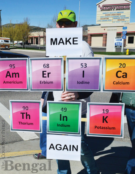 Man holding 'MAKE Am Er I Ca Th In K AGAIN' poster.