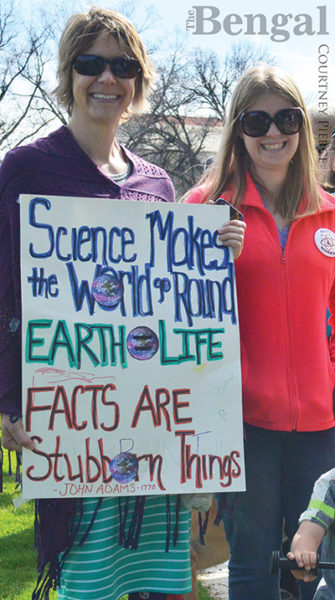 Women holding a poster with 'Science Makes the World go Round', 'EARTH = LIFE' and 'FACTS ARE Stubborn Things' (attributed to John Adams, 1770).
