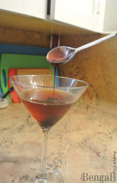 Adding a spoonful of maraschino juice to a Manhattan cocktail.