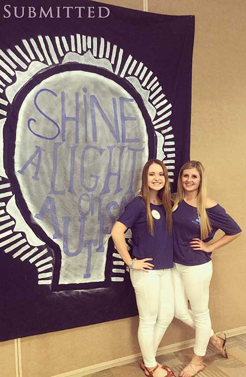 Two girls in front of a 'Shine a Light on Autism' sign