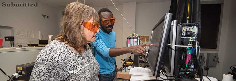 Woman and man in safety glasses looking at monitor.