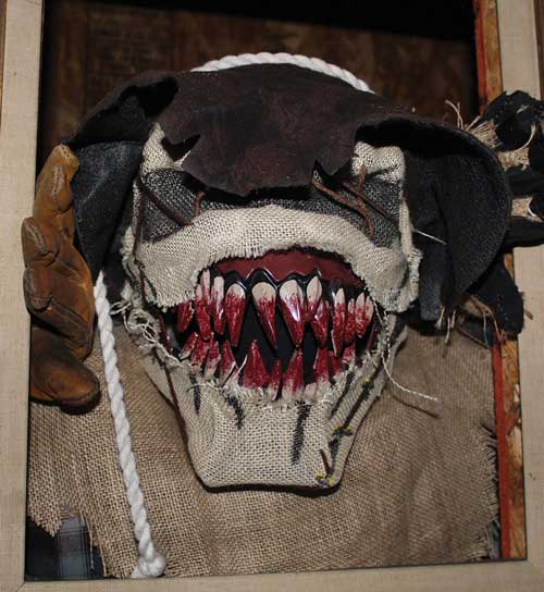 Man wearing monster mask grasps leans out window.