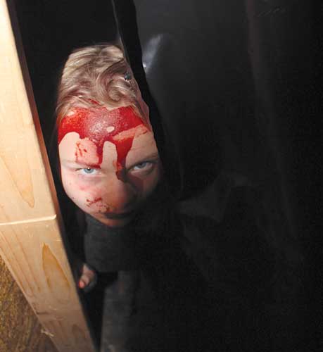 Girl with fake blood on face looks out from behind curtain.