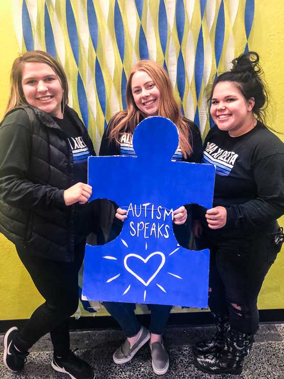 3 members of Alpha Xi Delta hold puzzle piece sign for Autism Speaks