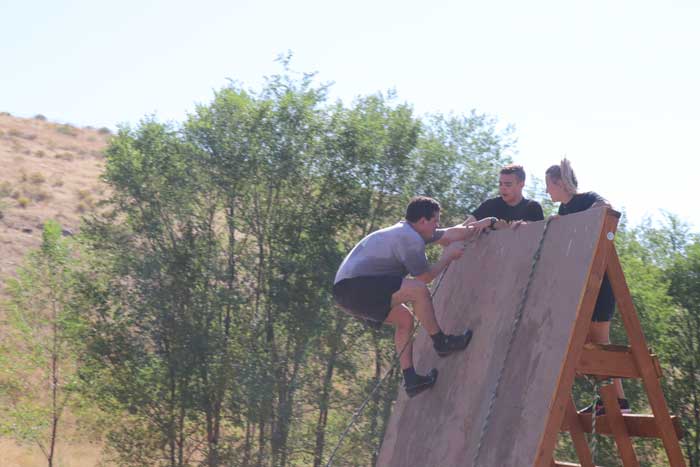 One participant climbs up wall while two others wait at top
