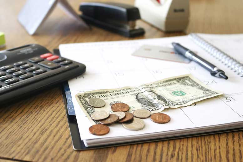 Spare change, a dollar bill, and a calculator rest on a notebook