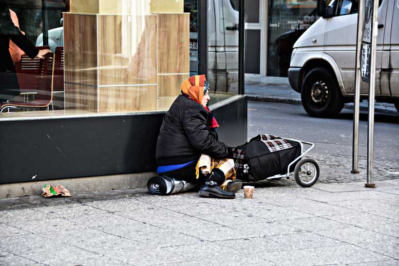 Homeless woman sits on street corner with belongings