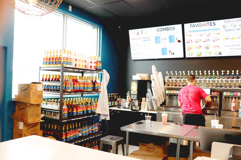 Man's back is to camera as he mixes drink with shelf of drink flavors next to him