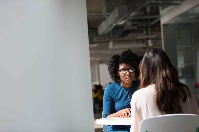 Two women sit facing each other and talking