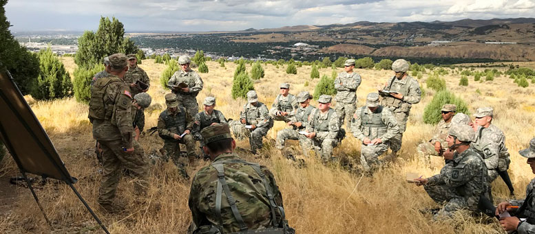 ROTC students in uniform stand and sit together in field