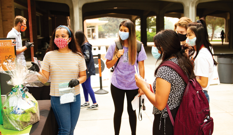 Multiple students wearing masks interact with other students outside.