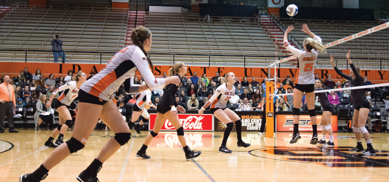 Image of ISU volleybal players paying. One ISU player is in mid air to set the ball. Another prepares to spike the ball. Other players are in motion around them.