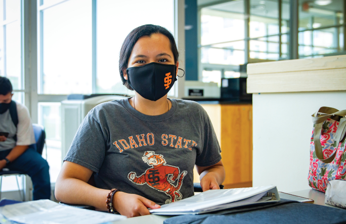 Image shows Joselynn Castillo, an ISU student sitting at a table in the PSUB wearing a black mask with and ISU logo on it.