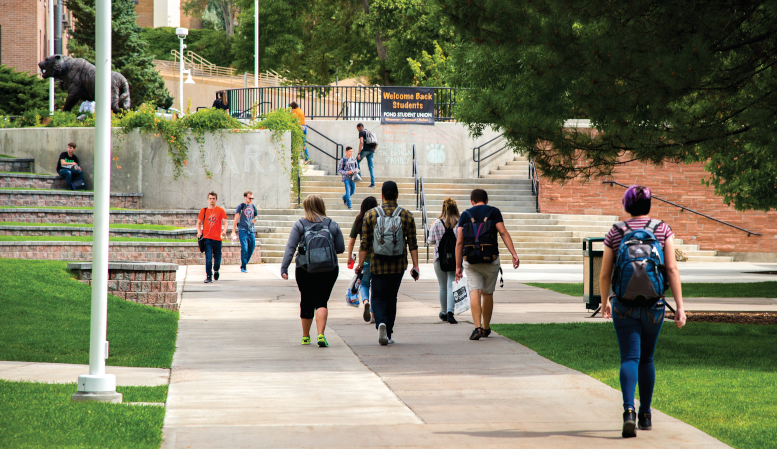 Image of multiple students walking across sidewalk outside of PSUB, most with their backs to the camera