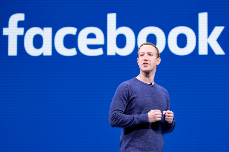 Mark Zuckerberg in front of blue Facebook logo