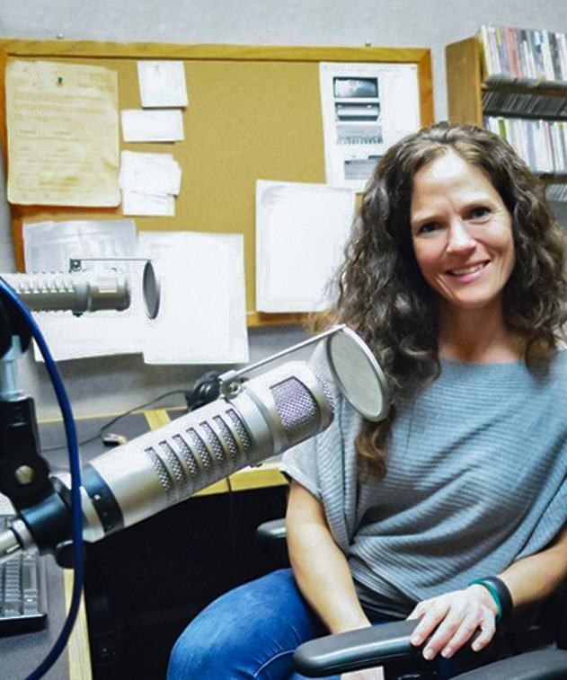 Elizabeth Brunner sits, turned and smiling at camera, with a microphone in front of her.