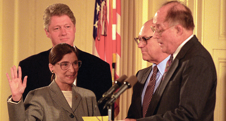 Ruth Bader Ginsburg sworn in with right hand raised. President Bill Clinton stands behind her and two men stand in front of her to the right