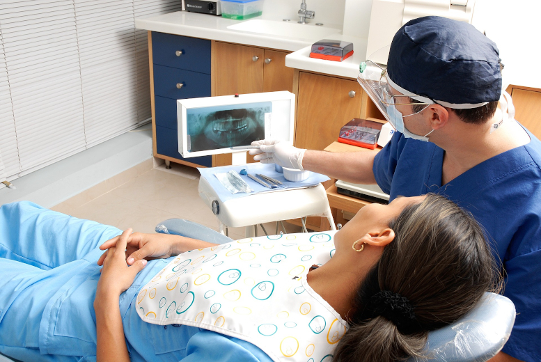 Dentist shows patient in sitting in dentist chair x-rays of her teeth.