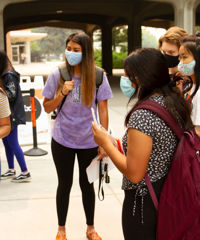 Students stand together talking, wearing masks