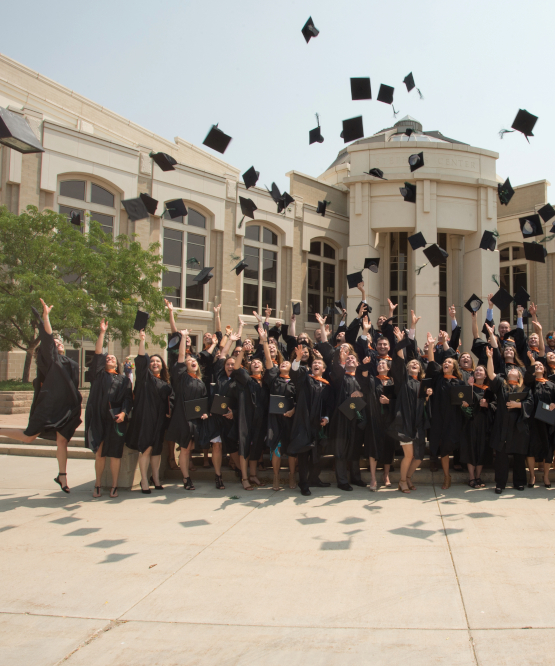 Crowd of ISU graduate thoss their caps while standing in front of the Stephen Performing Arts Center