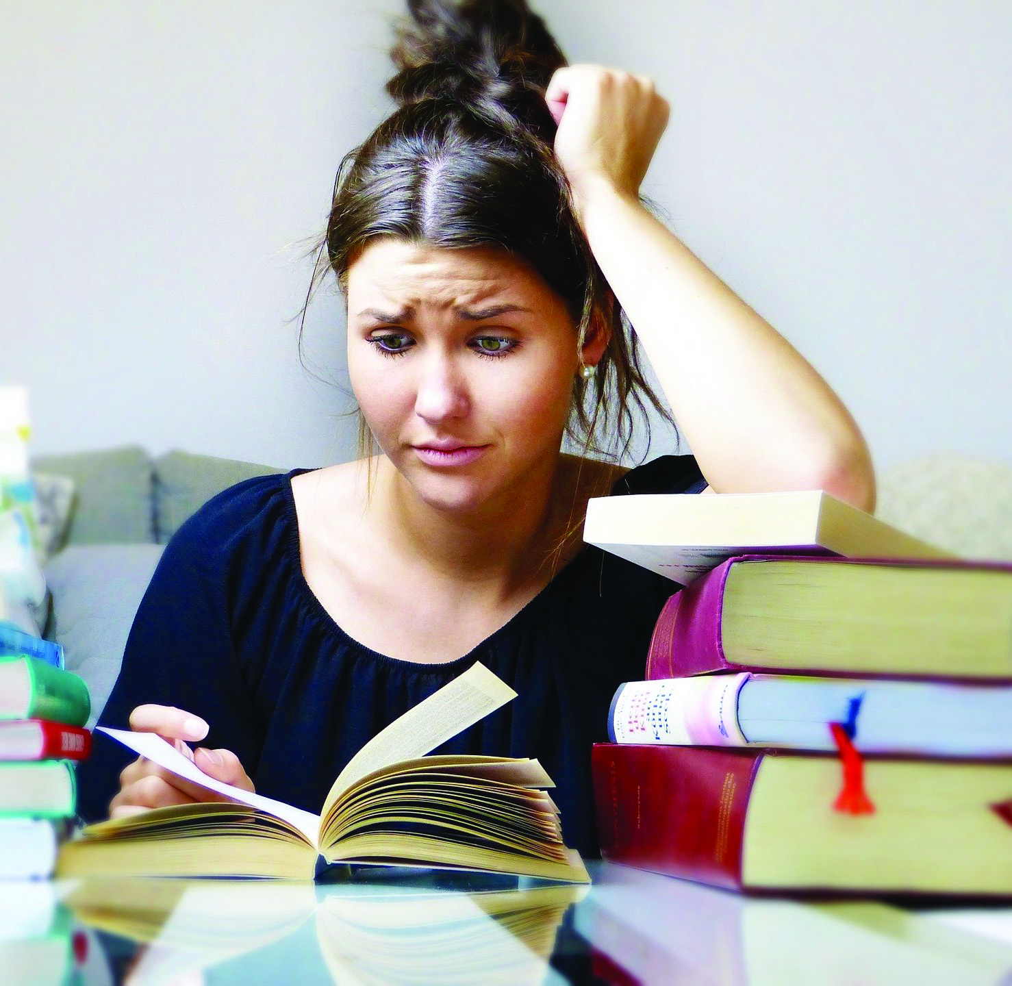 Woman sits at table surrounded by books, looking at open book with distressed face