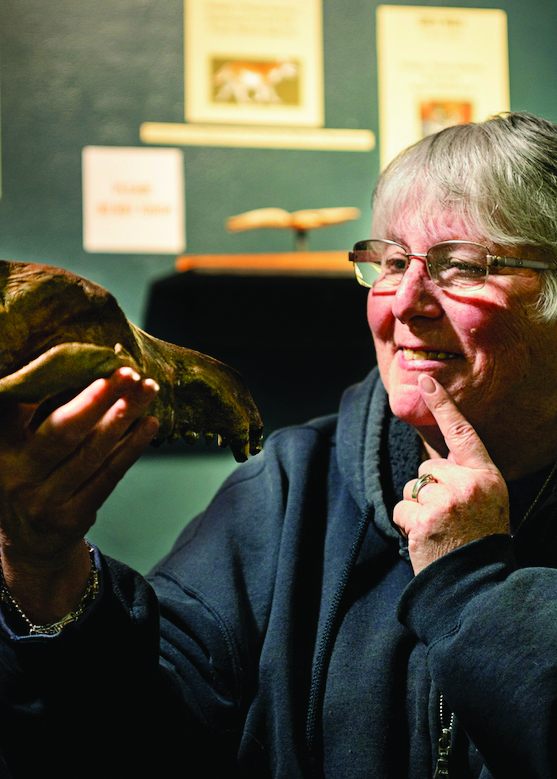 Featured: Mary Thompson holds Dire Wolf, looking at it and gesturing with a finger at her own teeth.