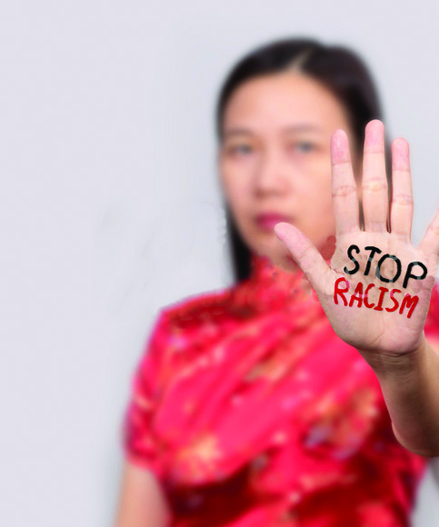 Asian woman holds her hand out, palm facing the camera. She is blurred in the background. Her hand is in focus and on it are the words "Stop Racism"