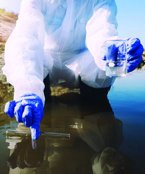 Person in coveralls and wearing gloves crouches in water testing it