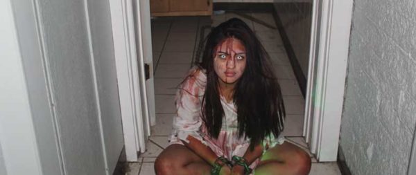 Girl in in raggedy clothes and fake blood on her face sits in hallway of haunted house