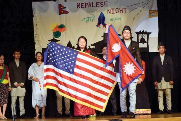 Two students hold American and Nepalese flags respectively while other students stand in background.