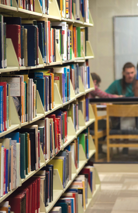 Shot of bookcase in library with students sitting at table in background