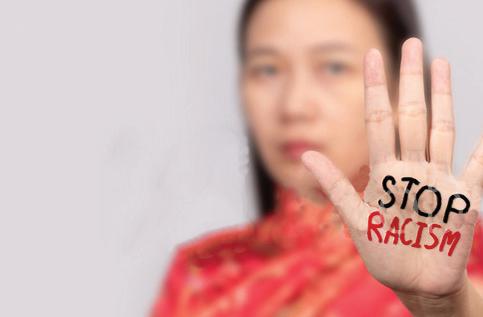 Asian woman holds her hand out, palm facing the camera. She is blurred in the background. Her hand is in focus and on it are the words "Stop Racism"